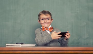 Young boy in bow-tie seated at a desk in front of a chalkboard